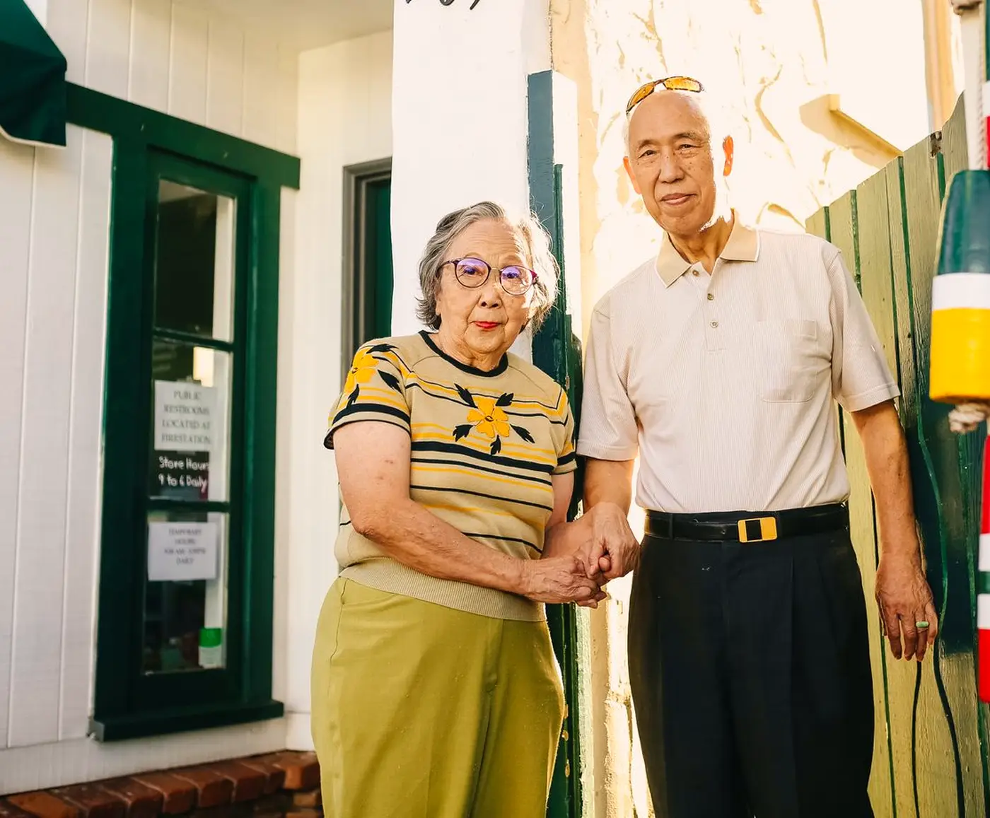 Smiling older Asian couple holding hands in front of their home